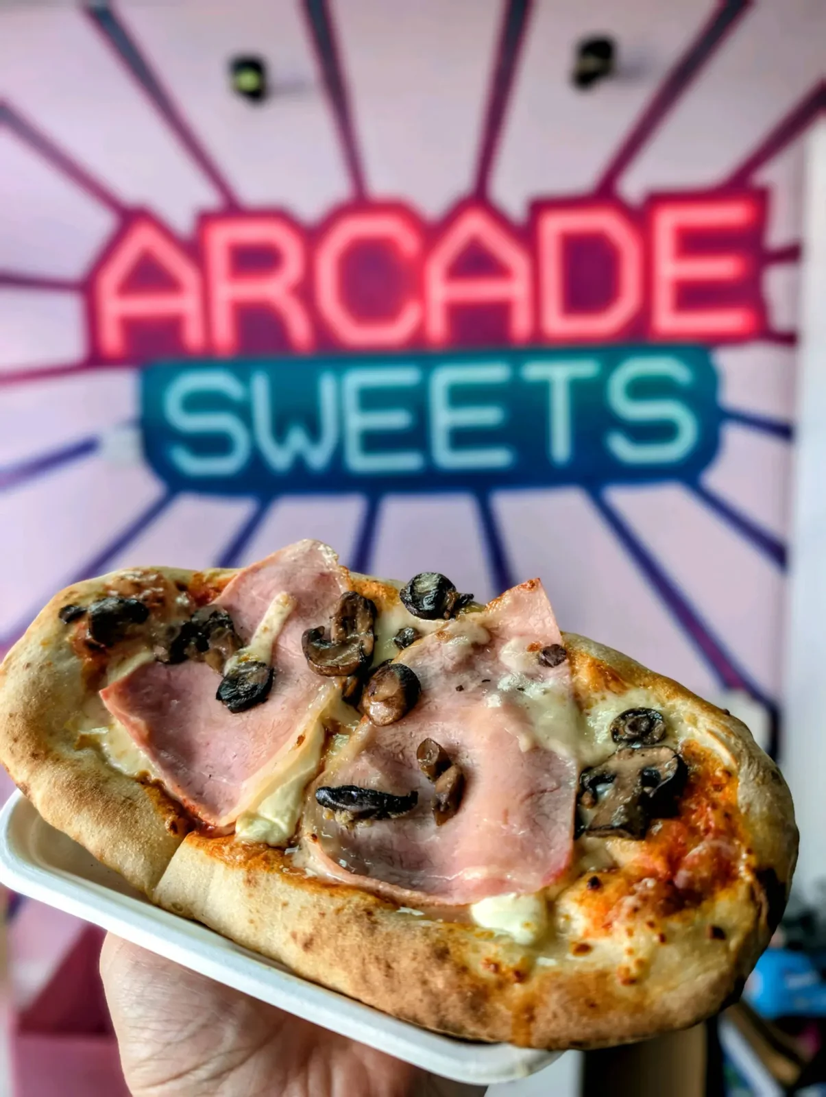 Pizza held in front of the Arcade Sweets sign